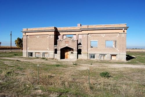 Abandoned brick school building with broken windows, set against a clear blue sky and grassy field.