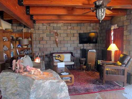 Cozy living room with stone walls, wooden beams, a guitar, and a mix of modern and rustic furniture.