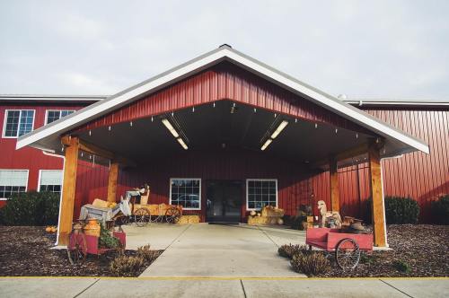 A red barn-style building with a covered entrance, featuring vintage farm equipment and decorative plants.