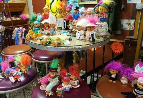 A colorful display of troll dolls with vibrant hair, arranged on a table in a cozy shop setting.