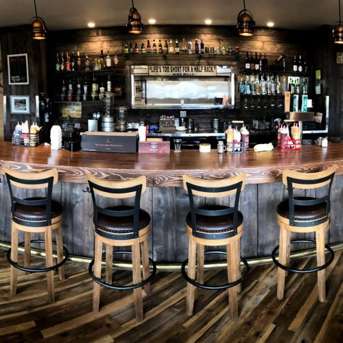A rustic bar with wooden stools, shelves of liquor, and a warm, inviting atmosphere.