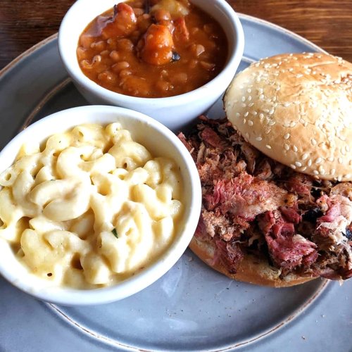A plate featuring a pulled pork sandwich, macaroni and cheese, and a bowl of baked beans.