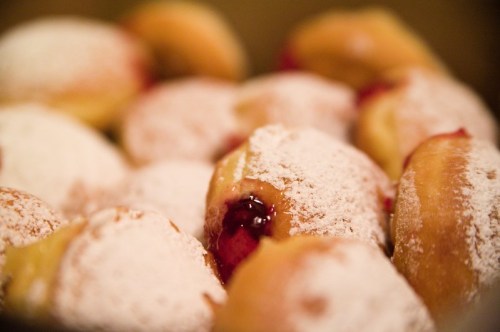 A close-up of powdered sugar-dusted doughnuts filled with red fruit jam.