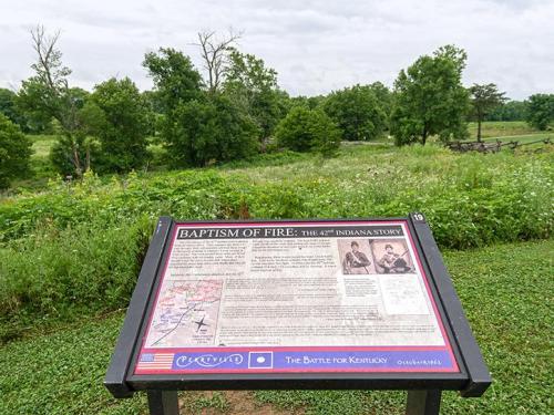 A historical marker titled "Baptism of Fire: The 49th Indiana Story" in a green landscape with trees and cloudy skies.