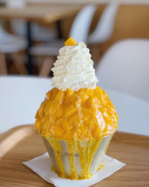 A delicious mango dessert topped with whipped cream and fresh mango chunks, served in a cup on a wooden tray.