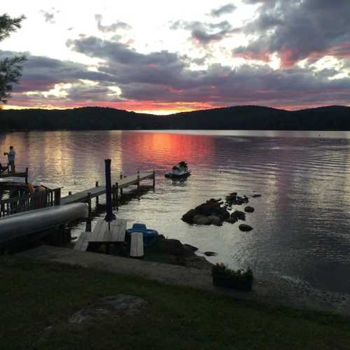 A serene lake at sunset, with colorful clouds reflecting on the water and a small boat in the distance.