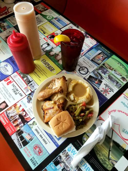 A plate of food with chicken, mashed potatoes, green beans, a roll, and a drink on a colorful table covered in ads.