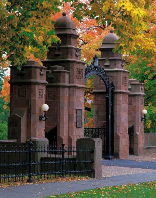 Historic stone gate with ornate ironwork, surrounded by vibrant autumn foliage in shades of orange and yellow.