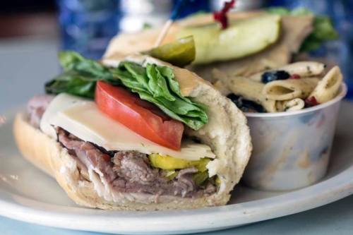 A hearty sandwich with roast beef, cheese, lettuce, tomato, and pickles, served with a side of pasta salad.