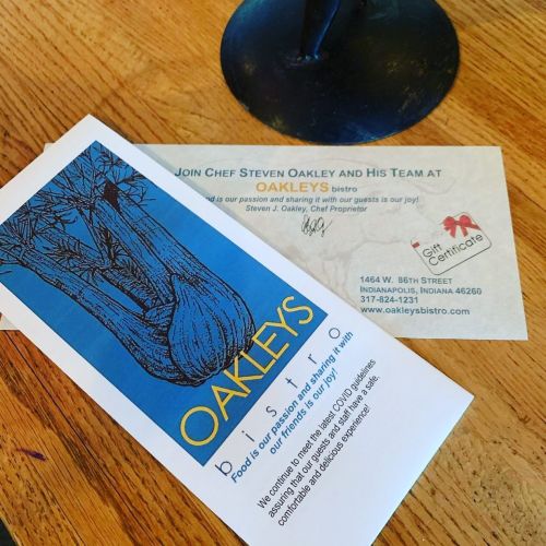 A menu from Oakley's Bistro featuring a blue illustration of garlic and a gift certificate on a wooden table.