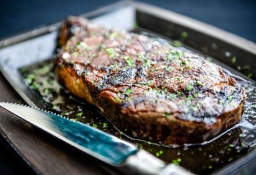 A perfectly cooked steak on a wooden platter, garnished with herbs and served with a knife beside it.