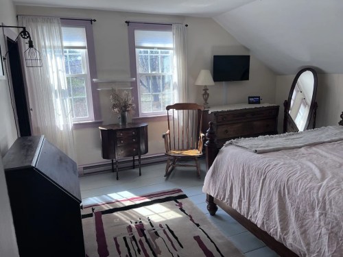 Cozy bedroom with a bed, wooden furniture, a rocking chair, and large windows letting in natural light.