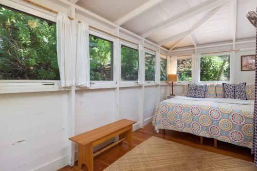 Cozy bedroom with a patterned bedspread, wooden bench, and large windows overlooking greenery.