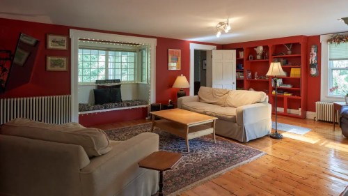 Cozy living room with red walls, a window seat, two sofas, a coffee table, and bookshelves filled with books.