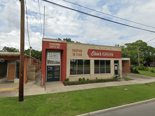 Exterior of Elise's Plate & Pie, a brick building with a sign, parking area, and green lawn under a cloudy sky.