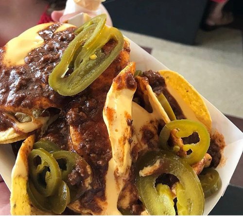 A close-up of nachos topped with cheese, chili, and jalapeños served in a white tray.