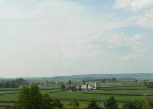 A scenic view of rolling green fields and a distant farm under a partly cloudy sky.