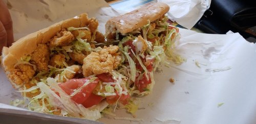 A sandwich filled with fried shrimp, lettuce, and tomato, served in a soft bun on a white paper surface.