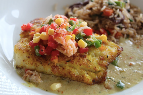 A plate featuring seasoned fish topped with colorful salsa, served with rice and beans on the side.