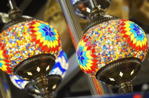 Colorful mosaic lamps with intricate patterns, hanging from a ceiling, creating a vibrant and warm atmosphere.