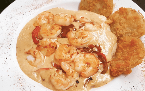 A plate of shrimp served over creamy grits, accompanied by two golden-brown fritters.