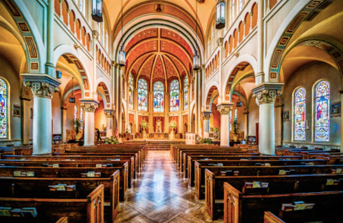 Interior of a grand church featuring wooden pews, stained glass windows, and a beautifully decorated altar.