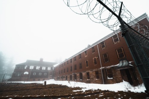 Abandoned building shrouded in fog, with barbed wire fence and snow-covered ground.