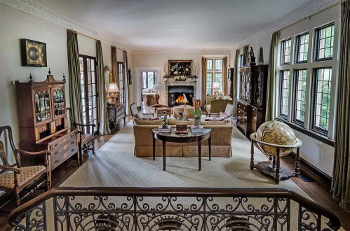 A cozy living room with a fireplace, elegant furniture, large windows, and a globe, viewed from an upper level.