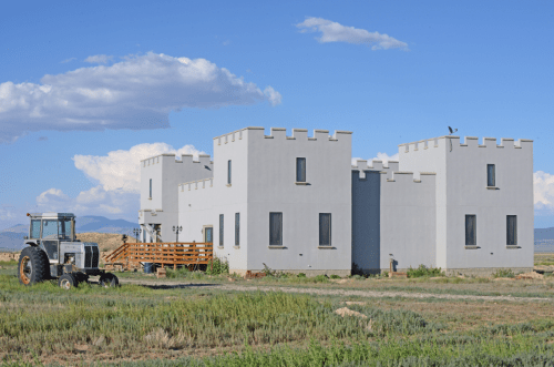 A modern castle-like building with a tractor in a grassy field under a blue sky with clouds.