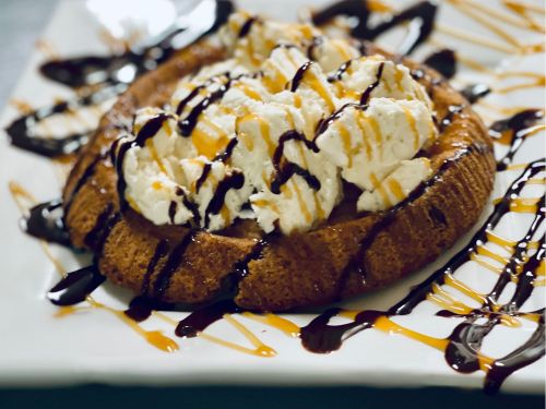 A warm dessert topped with whipped cream, chocolate, and caramel drizzles on a white plate.