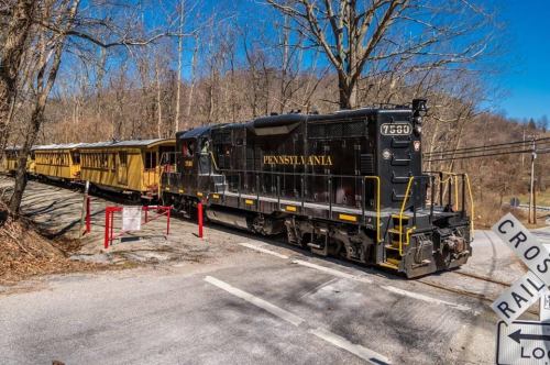 A black train engine labeled "PENNSYLVANIA" parked beside a yellow passenger car in a wooded area.