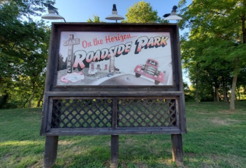 A vintage roadside park sign featuring a classic truck and a scenic background, surrounded by trees.