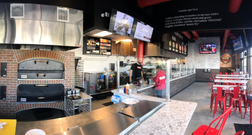A modern restaurant interior with a pizza oven, counter, and seating, featuring a staff member preparing food.