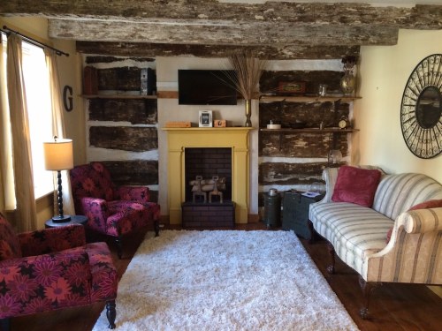 Cozy living room with a yellow fireplace, rustic wooden walls, plush seating, and a soft area rug.