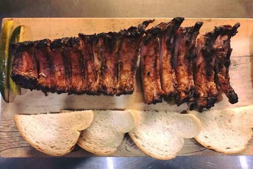 A wooden platter with grilled ribs and slices of white bread, garnished with a lime wedge.