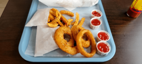 A tray with crinkle-cut fries, onion rings, and three cups of ketchup on a blue tray.