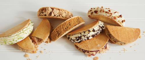 A variety of dessert sandwiches with different fillings, including cream and crumbled toppings, arranged on a white surface.