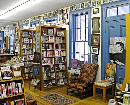 A cozy bookstore interior with bookshelves, framed photos on the walls, and a comfortable chair by the window.