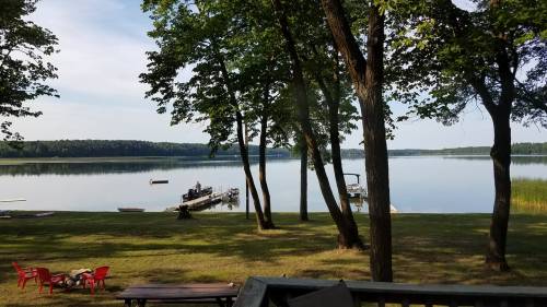 A serene lake view surrounded by trees, with boats docked and red chairs on the grassy shore.