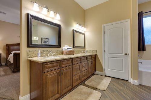 Spacious bathroom with dual sinks, wooden cabinetry, and two mirrors, featuring soft lighting and plush rugs.