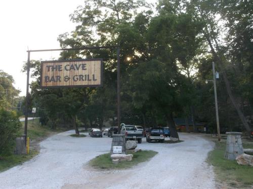 Sign for "The Cave Bar & Grill" at the entrance of a gravel driveway, surrounded by trees and parked cars.