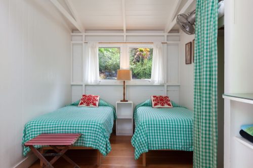 Cozy bedroom with two twin beds, green checkered bedding, a lamp, and a window overlooking greenery.