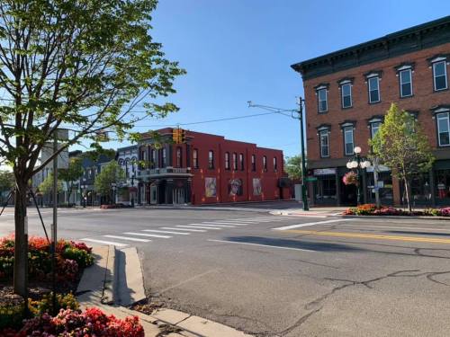 A sunny street view featuring colorful buildings, trees, and flower beds at an intersection.