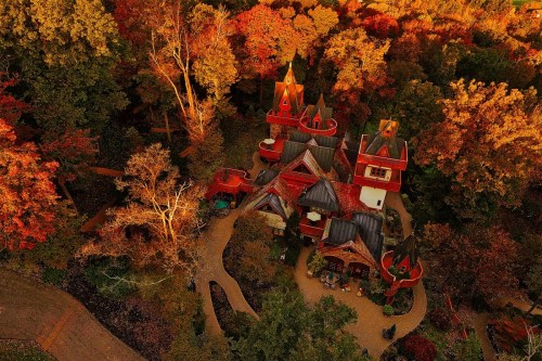 Aerial view of a whimsical, multi-turreted house surrounded by vibrant autumn foliage.