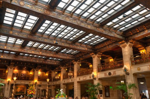 Ornate interior of a grand hall with a glass ceiling, intricate woodwork, and elegant decor.