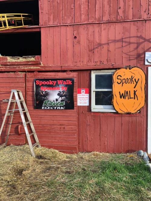 A red barn with a "Spooky Walk" sign and a ladder leaning against it, surrounded by hay.