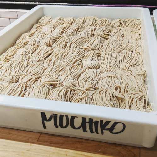 A large white tray filled with neatly arranged strands of uncooked mochiko noodles.