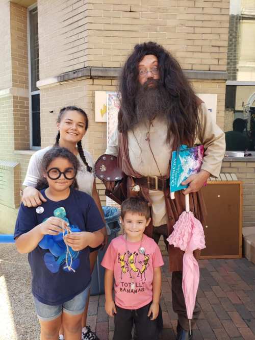 A group of three children and an adult dressed as a wizard, posing together outdoors with playful expressions.