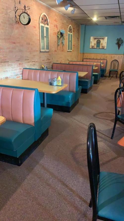 A cozy restaurant interior with teal and pink booths, wooden tables, and brick walls, creating a warm atmosphere.