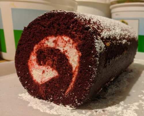 A red velvet cake roll dusted with powdered sugar, featuring a swirl pattern in the center.